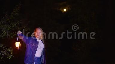 夜空中满月的可怕森林里拿着煤油灯的年轻女子。油灯惊魂女